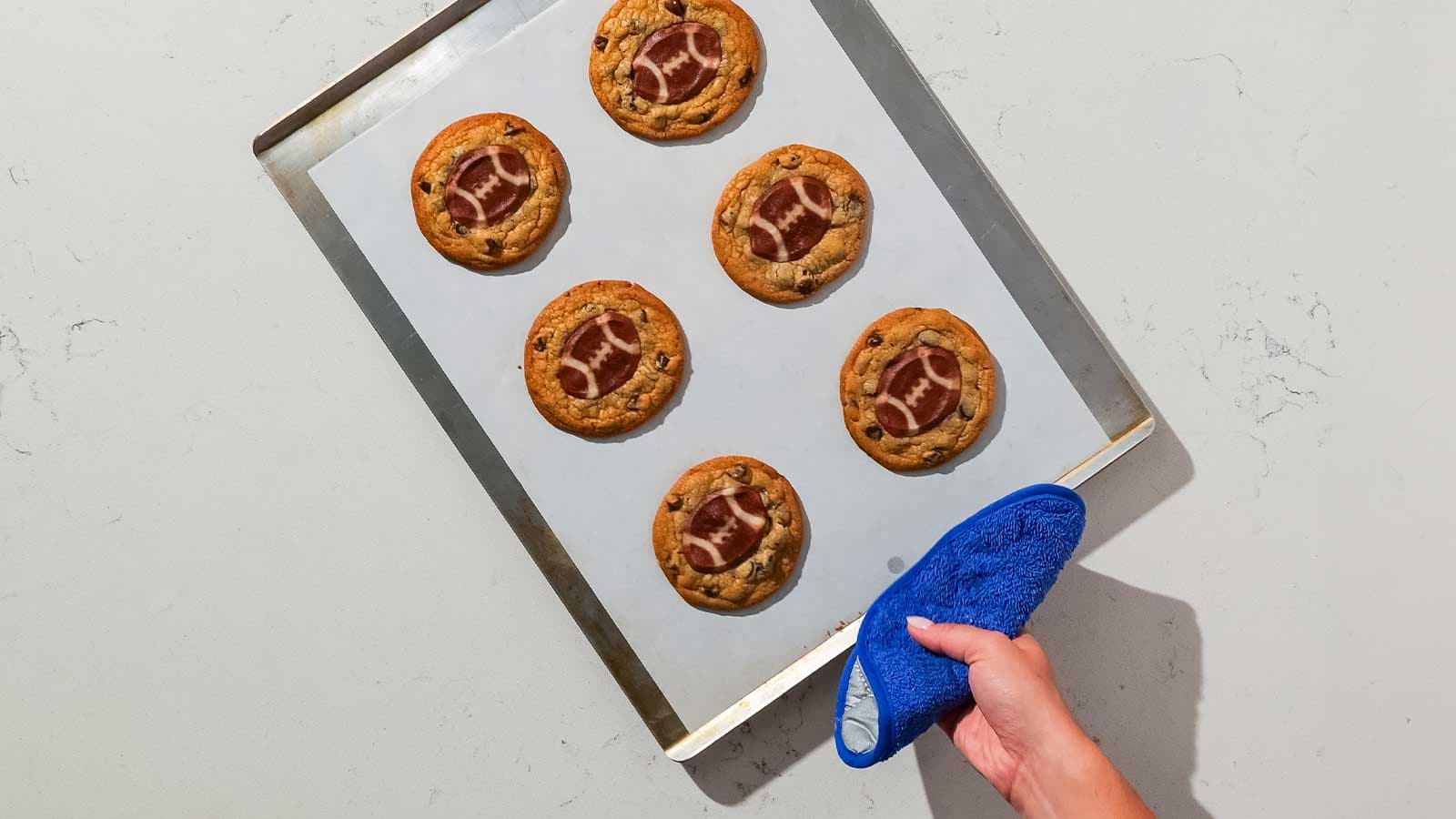 Person using a hot pad carrying a baking sheet with baked double stacked cookies.