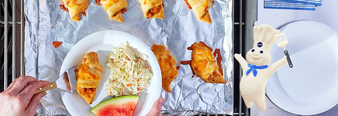 Golden-brown crescent rolls on grill, and a plate with coleslaw and watermelon nearby.